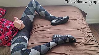 In a solo fetish scene, the transsexual shemale wears a plaid dress and argyle tights while jerking off her legs