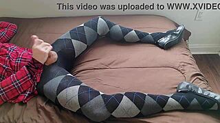 In a solo fetish scene, the transsexual shemale wears a plaid dress and argyle tights while jerking off her legs