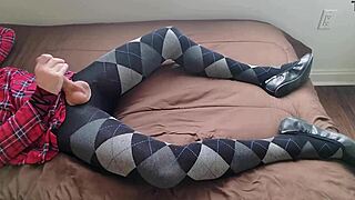 In a solo fetish scene, the transsexual shemale wears a plaid dress and argyle tights while jerking off her legs